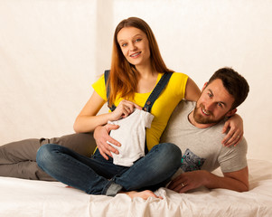 Beautiful coule  - young man and pregnant woman resting on bed holding babys dress