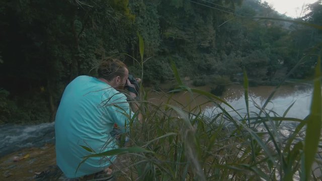 Man with a beard takes a picture of a waterfall