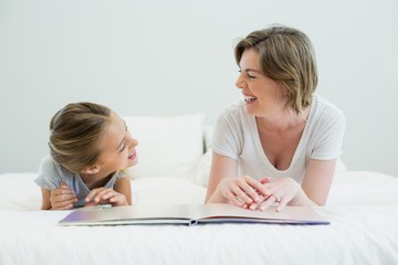 Mother and daughter lying on bed and reading book