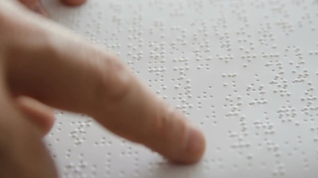 Hand of a blind person reading some braille text touching the relief.