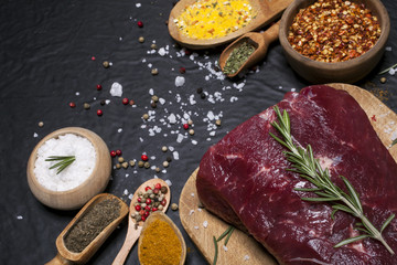 Raw beef steak on a cutting board with rosemary and spices.