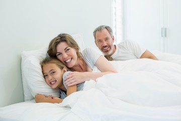 Obraz premium Happy family lying together on bed in bedroom at home
