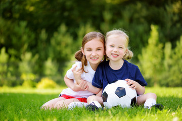Fototapeta premium Two cute little sisters having fun playing a soccer game on sunny summer day. Sport activities for children.