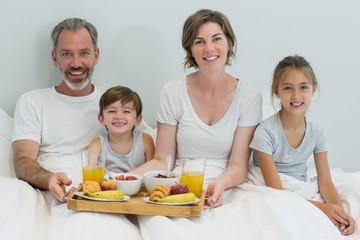 Portrait of smiling family having breakfast on bed in bedroom