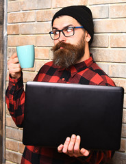 Bearded brutal caucasian hipster holding laptop with cup