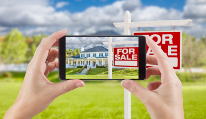 Female Hands Holding Smart Phone Displaying Photo of For Sale Real Estate Sign and House Behind.