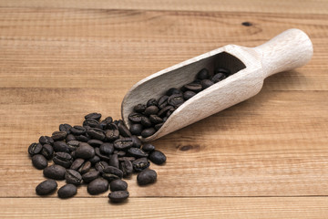 Coffee beans with wooden scoop on wooden table.