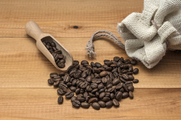 Coffee beans with wooden scoop on wooden table.