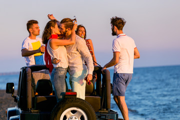 young group having fun on the beach and dancing in a convertible car