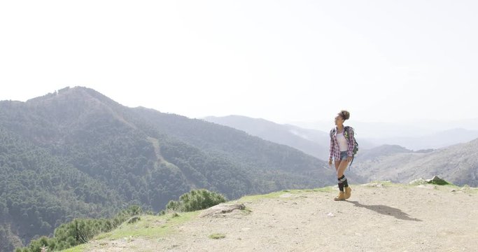 Young woman with backpack walking on top of mountain and looking around with beautiful views on background. 