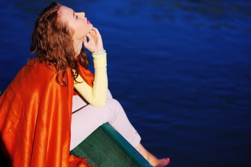 young beautiful woman sitting on the edge of the boat lowered feet in the water turned orange...
