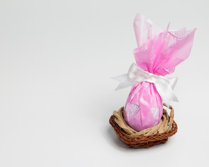 Chocolate Easter egg, pink packaging in basket. White background with copy space.