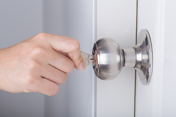 Hand use the key for unlocking door knob on white door