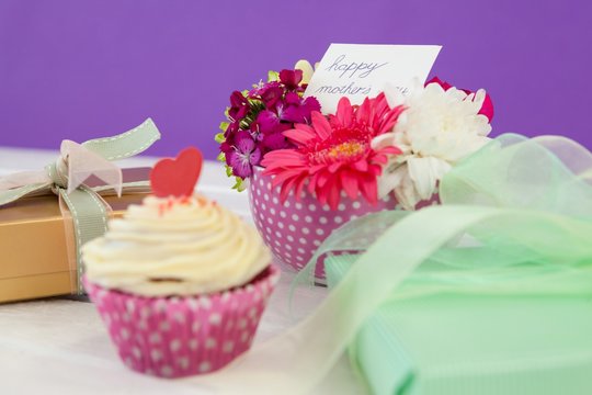 Cup cake, gift box and fresh flowers on wooden surface