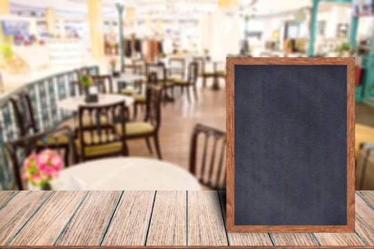 Chalkboard wood frame blackboard sign menu on wooden table, Blurred image background, Template mock up for adding your design and leave space beside frame for adding more text.