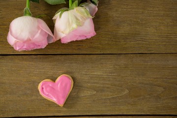 Pink roses with heart shape cookies on wooden plank