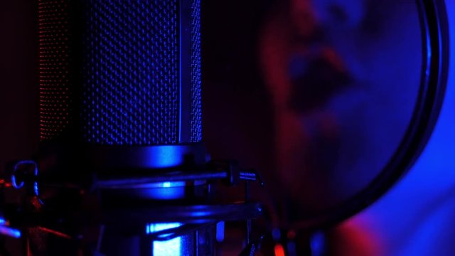 A young woman sings a song in a microphone in a recording studio under Neon light and a smoke machine