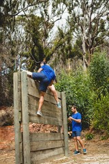 Obraz na płótnie Canvas Female trainer assisting man to climb a wooden wall