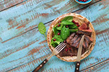 Plate with grilled steak, spinach, pomegranate on wooden blue table