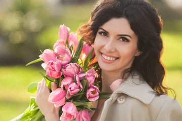 Fototapeta premium Closeup portrait of beautiful woman smiling with a braces holding bouquet of pink tulips and sitting in a park one spring day