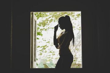Attractive woman looking at the sunrise standing near the window in her home.