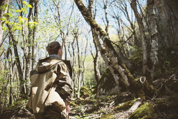 A young man in camp clothes and with a tail on his head looks and admires the greatness of nature, rocks and mountain forests