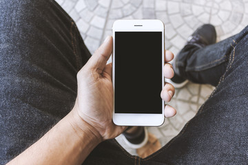 mockup image of hands holding white mobile phone with blank black screen, soft-focus in the background. over light and film colors tone