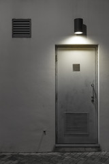 Light, air vent and door on wall at night