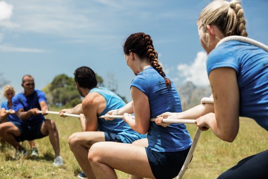 People playing tug of war during obstacle training course - Powered by Adobe