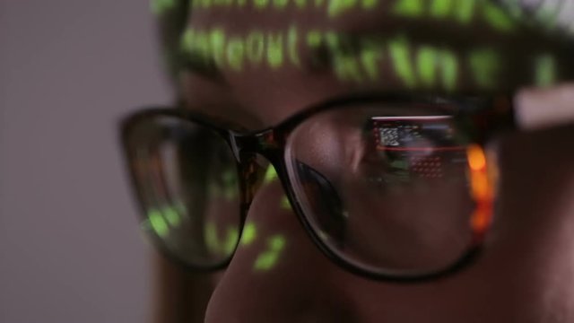 Computer screen reflected in hacker's glasses. Female hacker in dark working with data code.