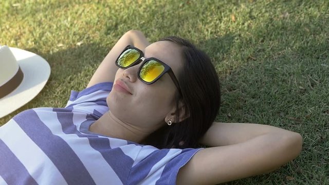 Happy Asian woman with sunglasses and white hat beside on green grass in public park
