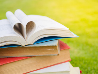 stack of books on table in garden with top one opened and pages forming heart shape