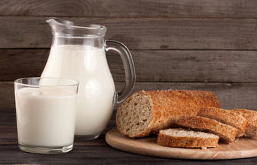 jug and glass of milk with a loaf of bread on a wooden background