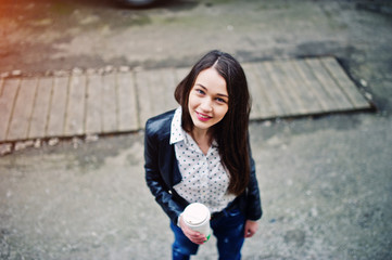 Portrait of stylish young girl wear on leather jacket and ripped jeans with cup of coffee. Street fashion model style.
