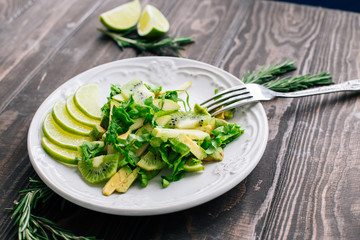 Healthy vegetarian food salad ingredients avocado, apples, kiwi, salad decorated with lime and rosemary on the wooden table