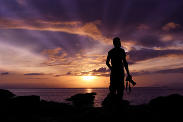 Silhouette photographer standing on the rocks by the sea with purple sky sunrise in the morning. 