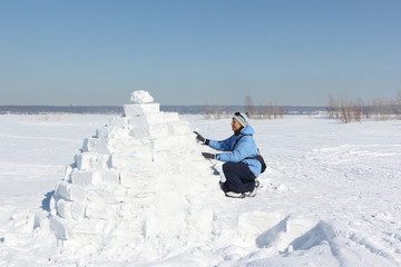 Woman in a blue jacket building an igloo on a snow glade in the winter