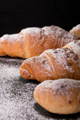 Croissant big and small with chocolate and powdered sugar on black background. French dessert