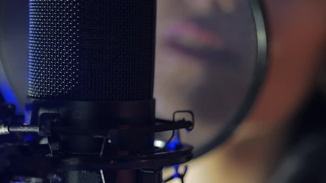 A young woman in earphones sings a song near a microphone in a recording studio under natural light