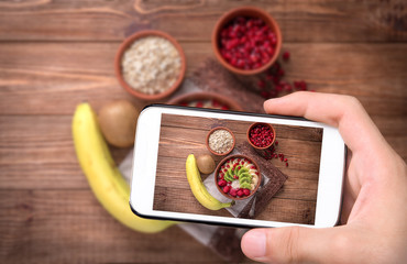 Fototapeta na wymiar Hands taking photo oatmeal porridge with banana, kiwi fruit , raspberries with smartphone.