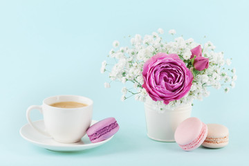 Fototapeta na wymiar Beautiful pink rose flower and gypsophilla in vase, macaroon and cup of coffee on turquoise vintage table for cozy breakfast.
