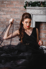 beautiful brunette girl with red lips manicure in a long black dress with a veil sitting on the floor keeps looking down close-up portrait