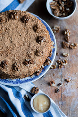 round delicious honey cake in blue white plate on a brown wooden background, bright flour, walnuts, white blue stripe kitchen towel amber Golden honey