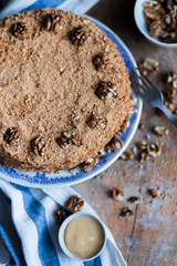 round delicious honey cake in blue white plate on a brown wooden background, bright flour, walnuts with white blue striped tea towel Golden amber honey with a fork
