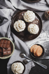 chocolate cupcakes with white cream s brown ceramic plate of ginger biscuits and chocolate spoons on the table with a kitchen towel food photo close-up