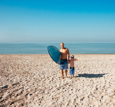 Surfer and his son are going to surf in the ocean in a sunny day