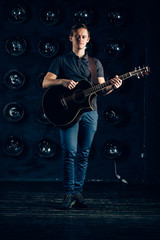 Fototapeta premium handsome guy guitarist blonde standing in the dark in a room with lamps