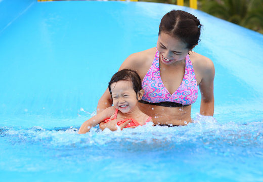 Pretty little girl with her mother sliding in swimming pool outdoors