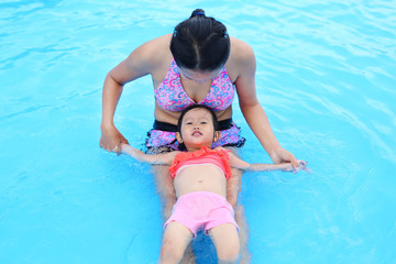 Pretty little girl with her mother sliding in swimming pool outdoors