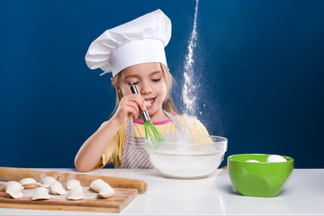 The little girl is cooking and preparing food on blue background